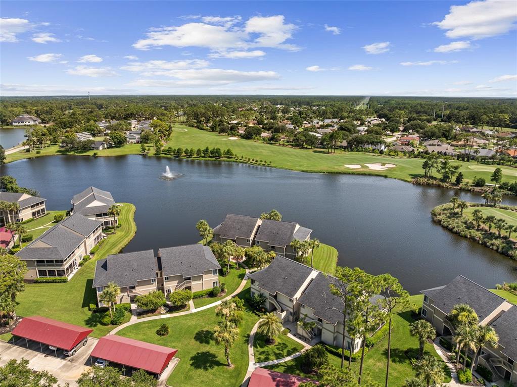 An aerial view shows apartment buildings with red carports situated beside a lake and golf course — 18 MAGNOLIA DRIVE S UNIT B, ORMOND BEACH, FL