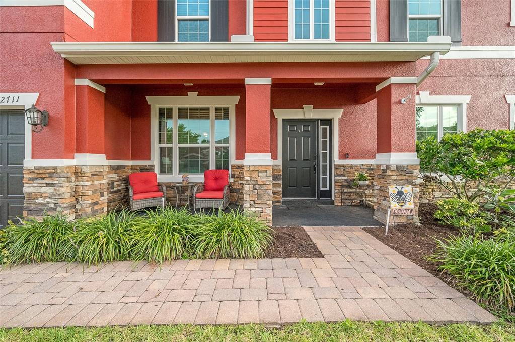 A red house exterior features a stone-accented porch with two chairs and a walkway — 2711 CYPRESS TREE TRAIL, ST CLOUD, FL