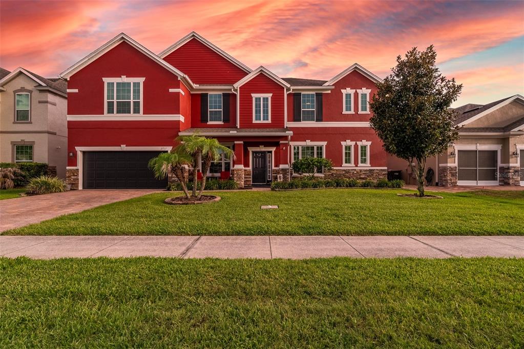 A two-story red house with a stone base and a front-facing garage at sunset — 2711 CYPRESS TREE TRAIL, ST CLOUD, FL