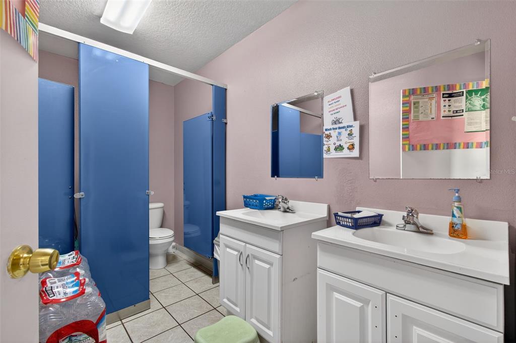 A bathroom features two white vanities, blue stall partitions, and a toilet on tiled flooring — 951 E HATHAWAY AVENUE, BRONSON, FL