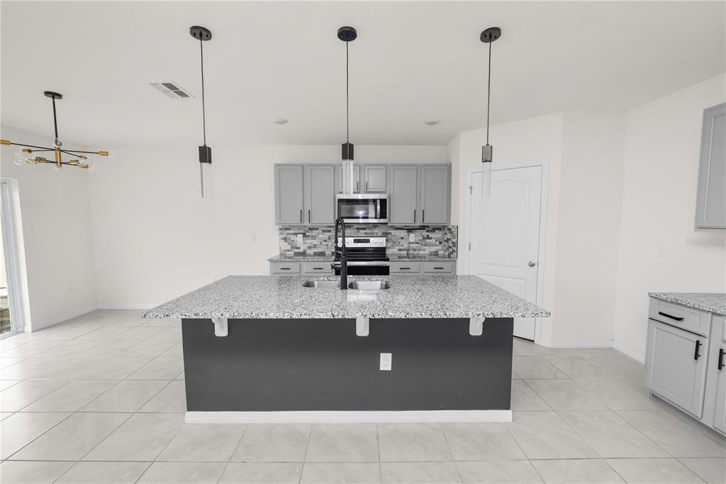 A kitchen features a large granite-topped island, gray cabinetry, stainless steel appliances, and tile flooring — 3935 PALAZZO PLACE, WINTER HAVEN, FL