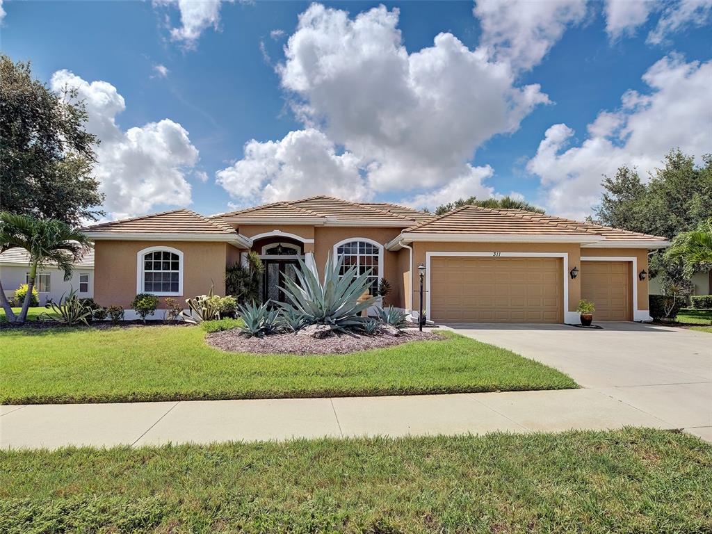 A single-story tan house with a tile roof, three-car garage, and a landscaped front yard — 311 WILD PINE WAY, VENICE, FL