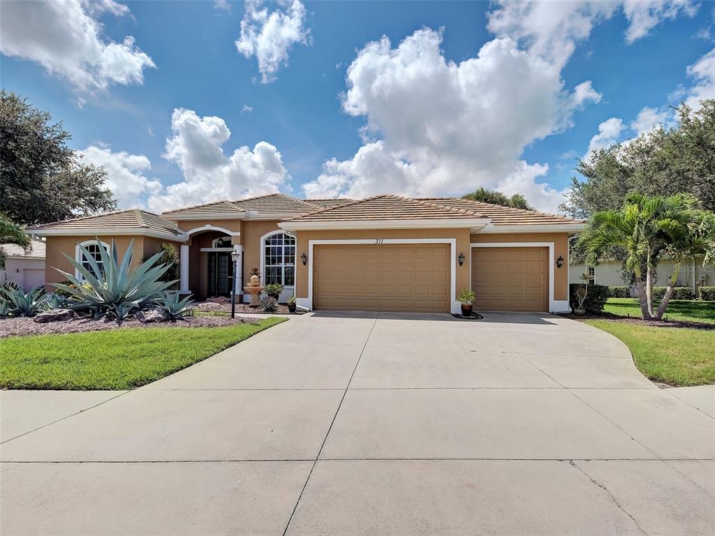 A single-story house with a tan stucco exterior, a tile roof, and a three-car garage — 311 WILD PINE WAY, VENICE, FL