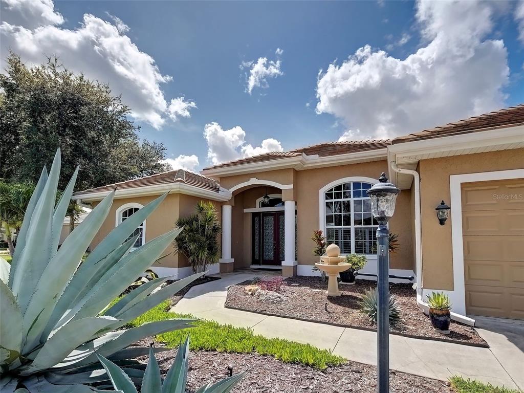 A tan single-story house features a front walkway, a small fountain, and a large agave — 311 WILD PINE WAY, VENICE, FL