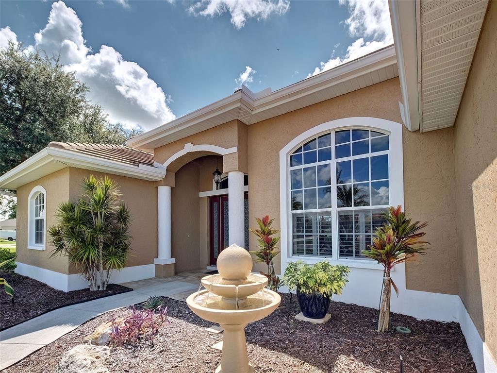 A tan stucco house exterior features a stone fountain, arched window, and covered entryway — 311 WILD PINE WAY, VENICE, FL