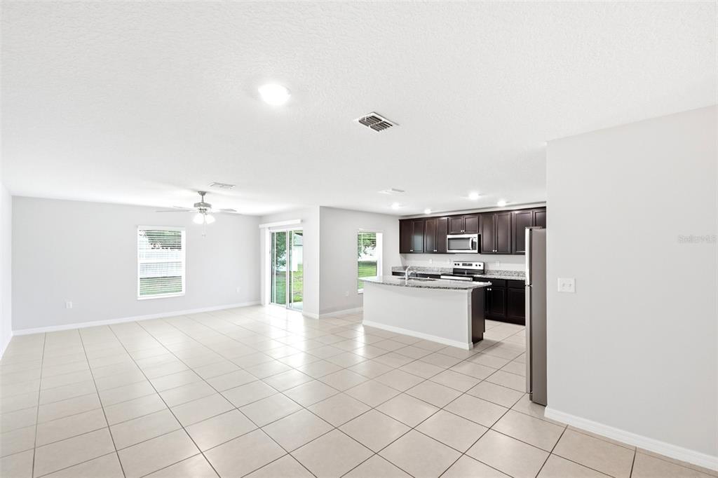 An open-concept living area features light tile flooring, a kitchen with dark cabinets, and sliding doors — 1668 GOPHER TREE STREET, MASCOTTE, FL