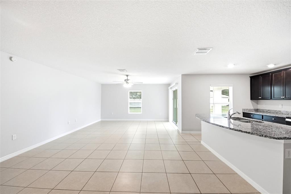 An open-concept living area features light tile flooring, a kitchen with granite countertops, and cabinetry — 1668 GOPHER TREE STREET, MASCOTTE, FL