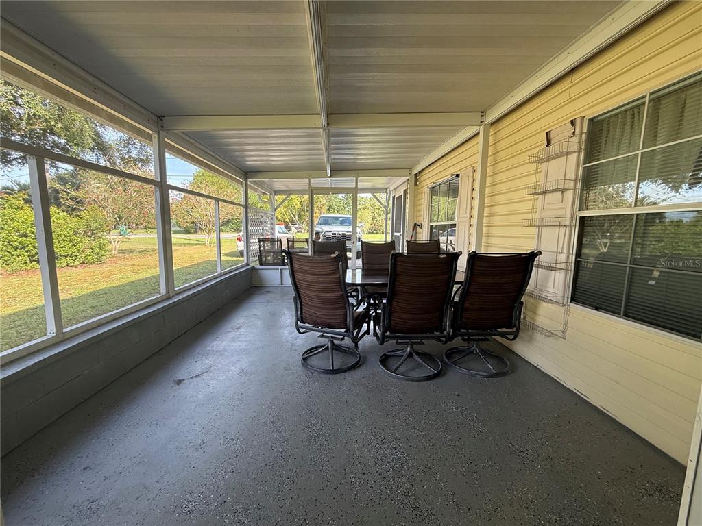 A screened-in porch features a concrete floor, outdoor dining furniture, and yellow siding — 8285 COUNTY ROAD 109B, LADY LAKE, FL