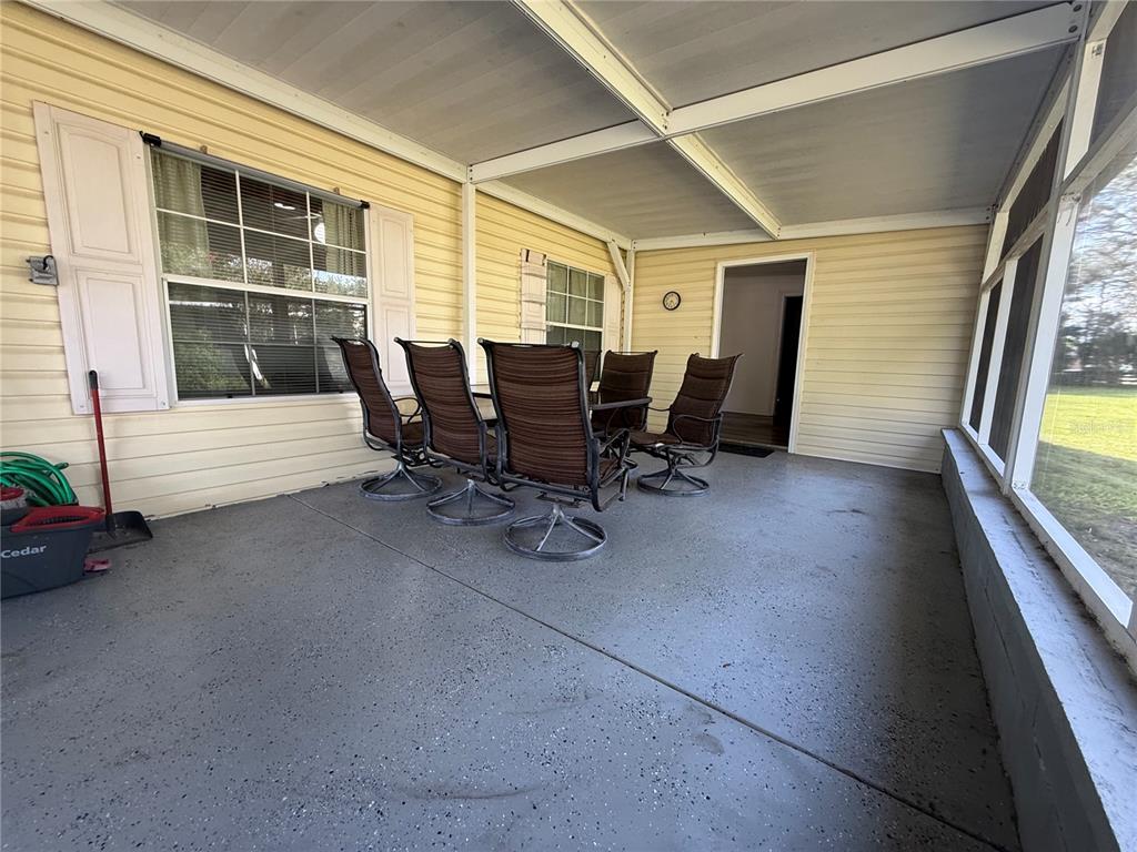 A screened-in porch features a gray concrete floor, yellow siding, and a dining set — 8285 COUNTY ROAD 109B, LADY LAKE, FL