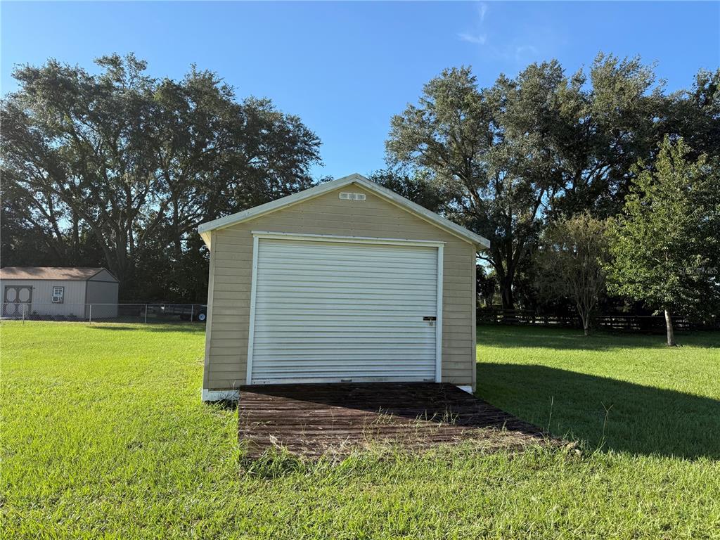 A tan storage shed with a roll-up door sits on a wooden platform in a yard — 8285 COUNTY ROAD 109B, LADY LAKE, FL