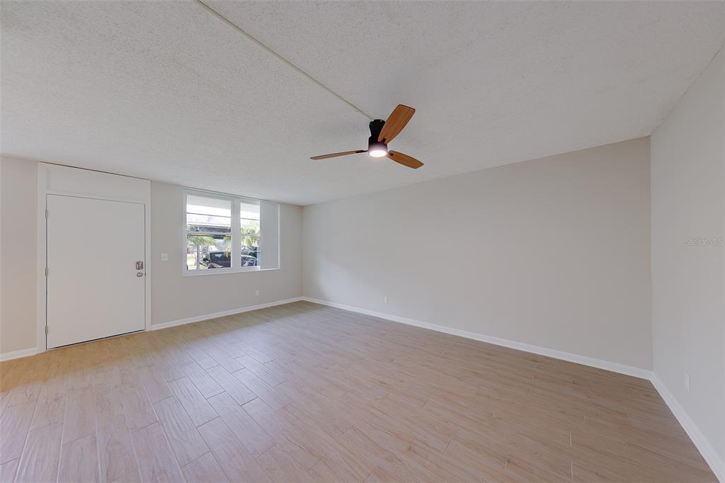 A living room features light wood-look tile flooring, beige walls, and a ceiling fan — 4715 BAY STREET NE UNIT 132, ST PETERSBURG, FL