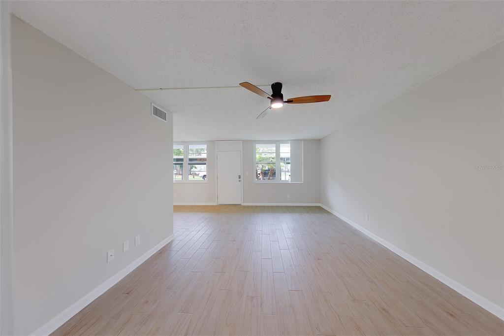 An empty living room features light wood-look flooring, neutral walls, and a ceiling fan — 4715 BAY STREET NE UNIT 132, ST PETERSBURG, FL