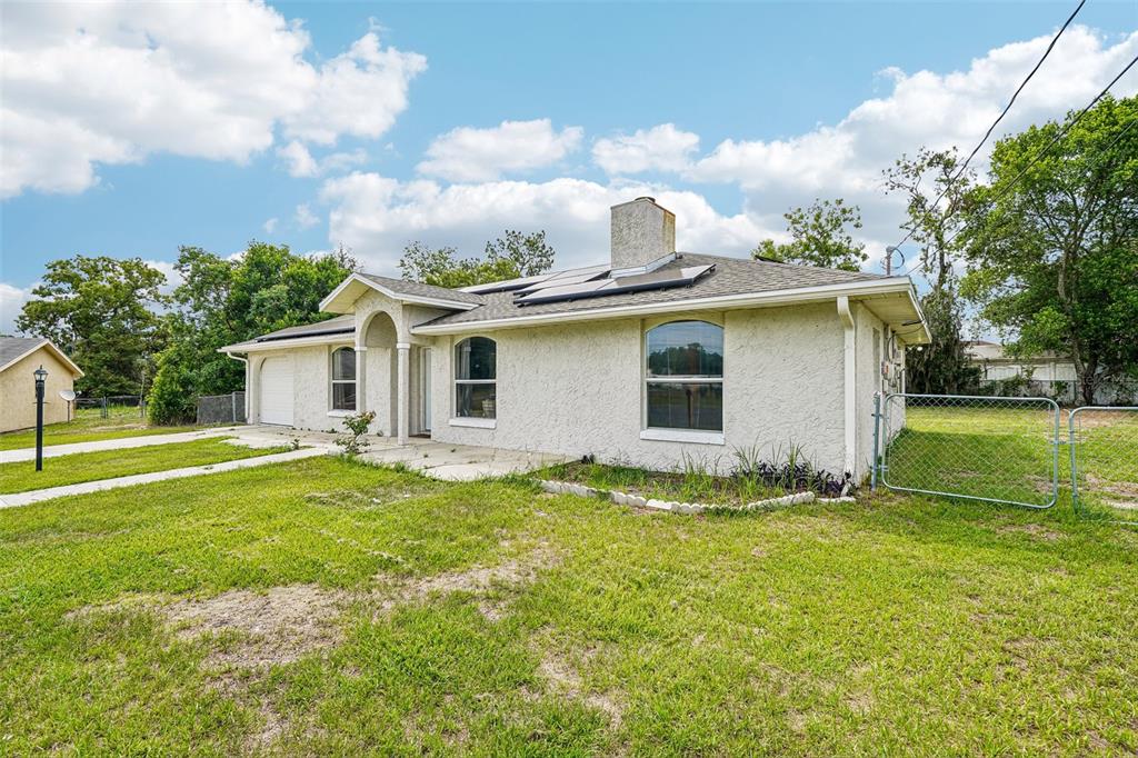A single-story stucco house with a chimney, solar panels, and a chain-link fenced yard — 18 SPRING RADIAL, OCALA, FL