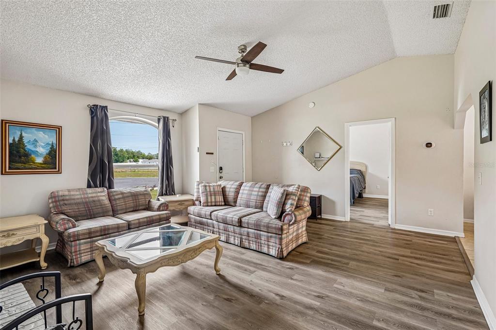 A living room features a vaulted ceiling, plaid sofas, a coffee table, and wood-look flooring — 18 SPRING RADIAL, OCALA, FL
