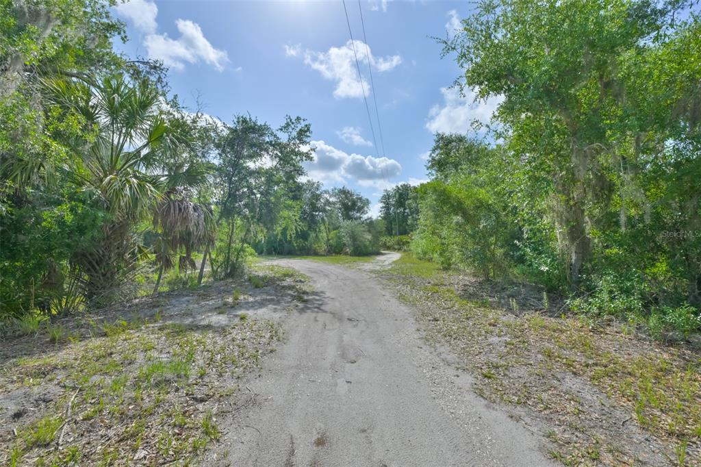 A yellow single-story house sits behind a chain-link fence with a wooden overhead gate — 14451 HIGHLAND ROAD, WIMAUMA, FL