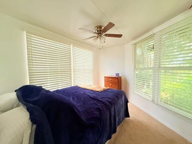 A bedroom features a bed with a blue blanket, a ceiling fan, and large windows — 2215 73RD STREET E UNIT 315, PALMETTO, FL