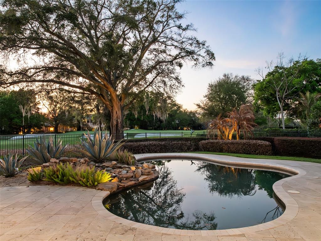 A backyard swimming pool with a stone rock feature overlooks a golf course at sunset — 5151 LATROBE DR, WINDERMERE, FL