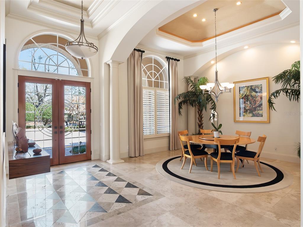 A foyer and dining area feature stone floors, arched windows, and a circular dining table — 5151 LATROBE DR, WINDERMERE, FL