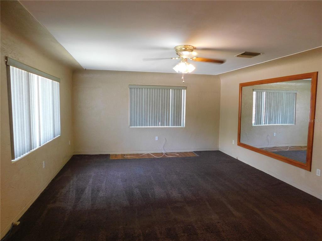 A living room features dark carpeting, beige walls, vertical blinds, a ceiling fan, and a mirror — 5430 2ND AVENUE N, ST PETERSBURG, FL