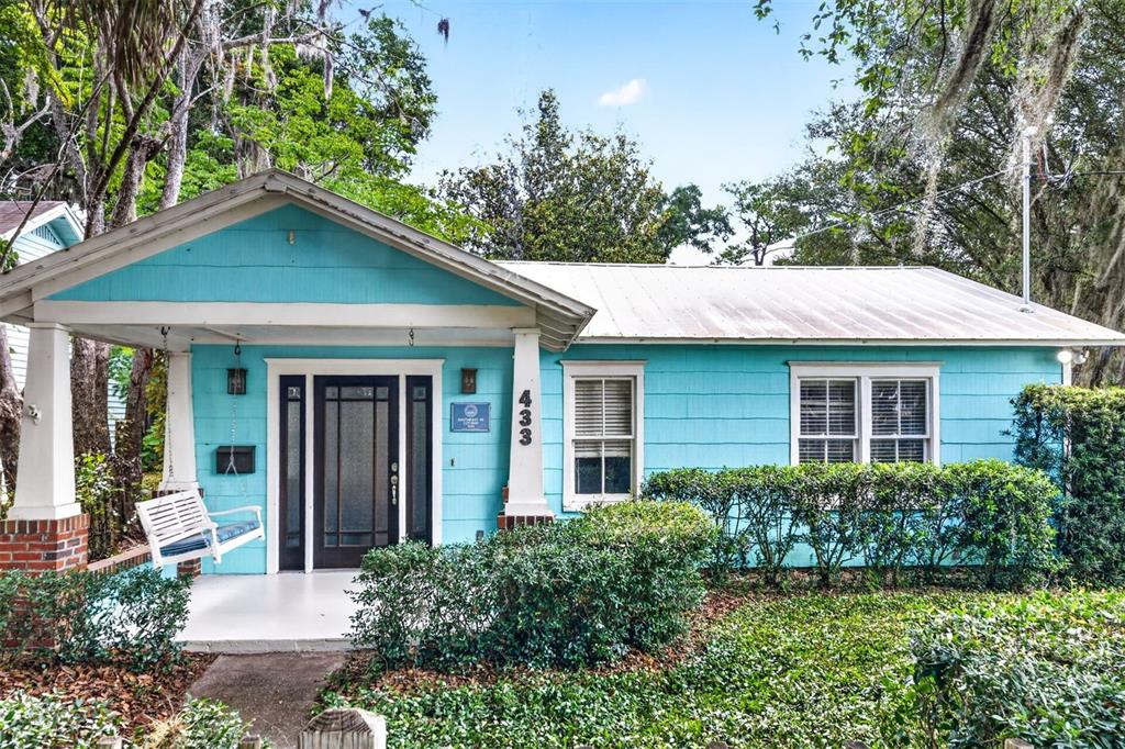 A turquoise cottage features a front porch with a white swing and a metal roof — 433 SE 7TH STREET, GAINESVILLE, FL