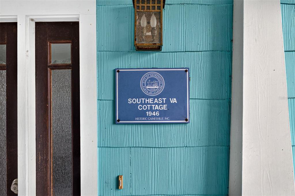 A blue historic plaque is mounted on the turquoise exterior siding next to a door — 433 SE 7TH STREET, GAINESVILLE, FL