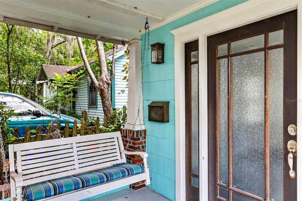 A white porch swing sits on a covered porch with turquoise siding and a glass door — 433 SE 7TH STREET, GAINESVILLE, FL