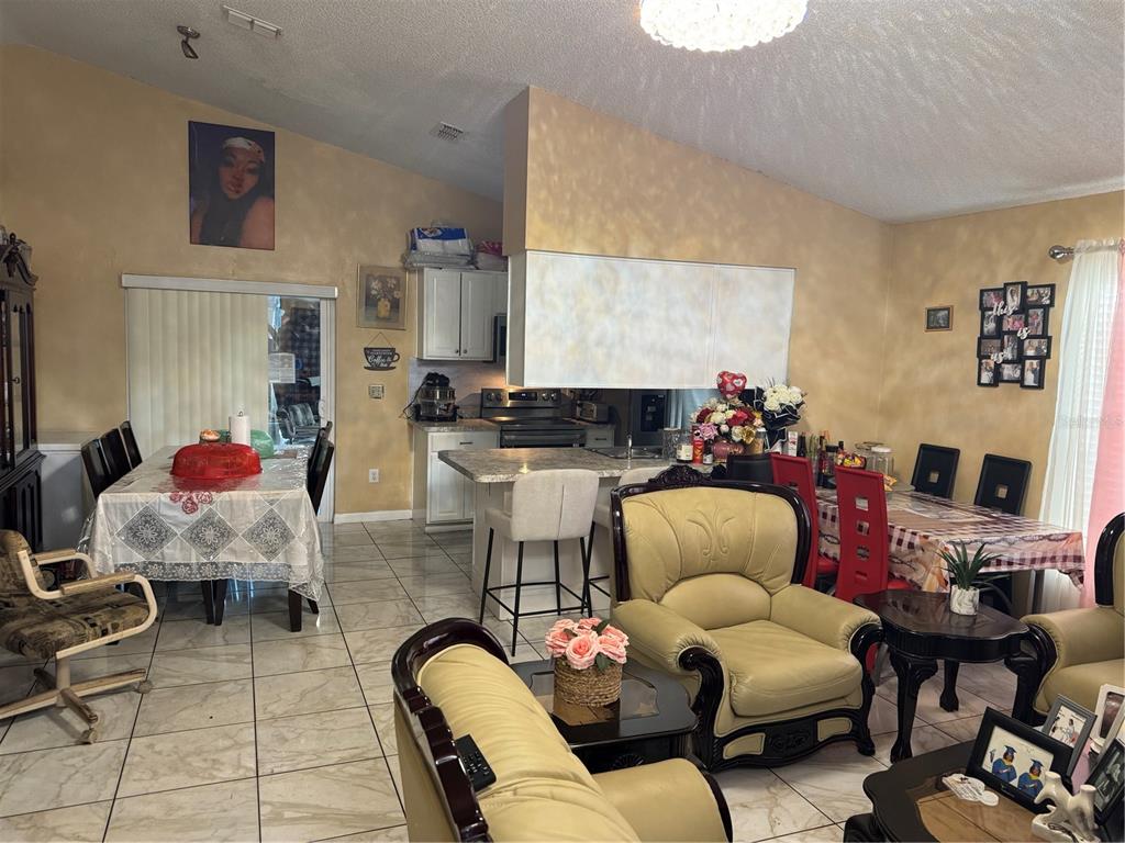 An open-concept living and dining area features tiled floors, a kitchen island, and vaulted ceilings — 3407 LAKE TINY CIRCLE, ORLANDO, FL