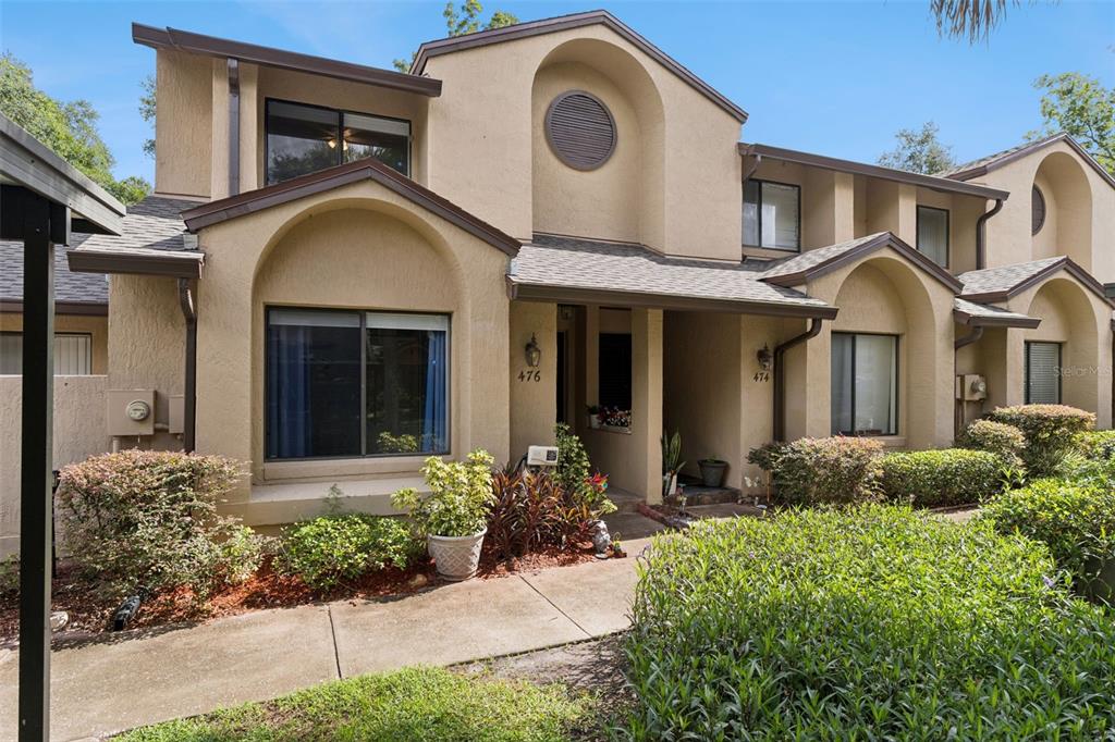 An exterior view of a multi-story tan stucco townhouse with a shingled roof — 476 CLUB DRIVE, WINTER SPRINGS, FL