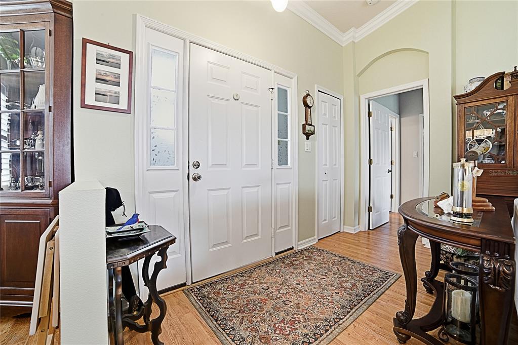 An entryway features a white front door, hardwood floors, a patterned rug, and wooden furniture — 3550 HUNTSVILLE LANE, LEESBURG, FL