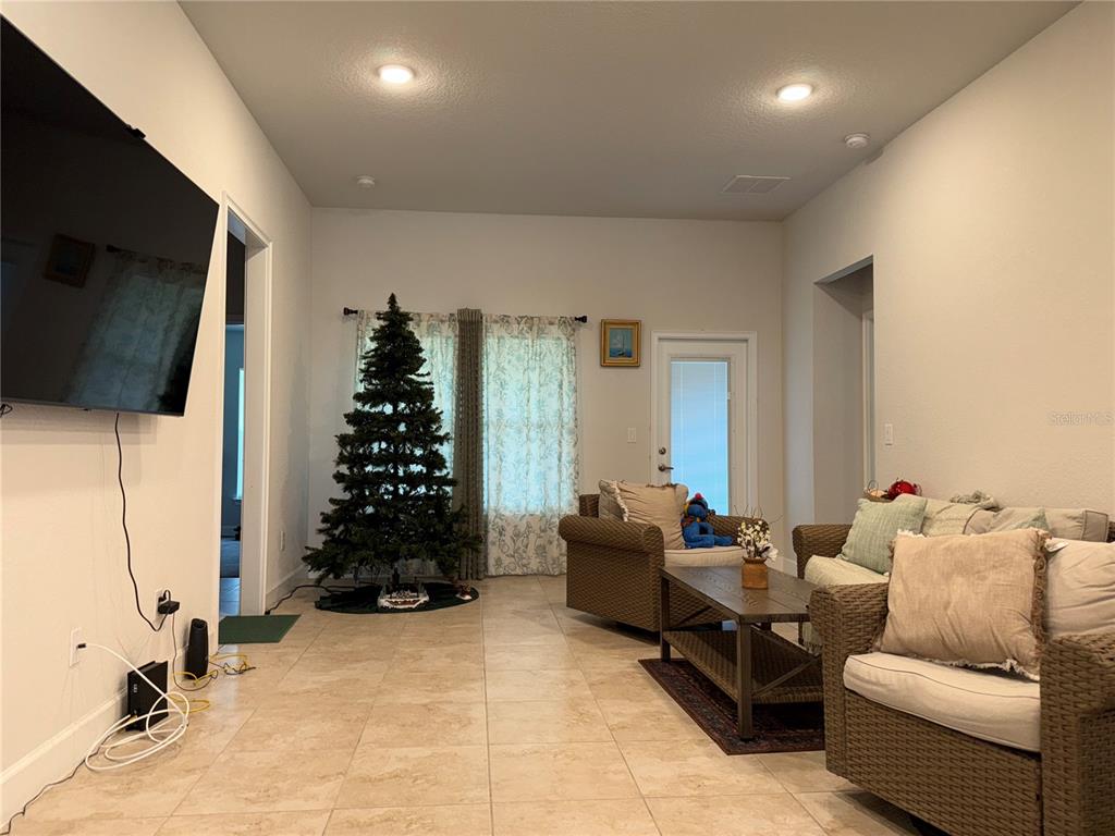 A living room features tile flooring, a Christmas tree, wicker furniture, and a wall-mounted television — 14921 TROPICAL VIOLET WAY, WIMAUMA, FL