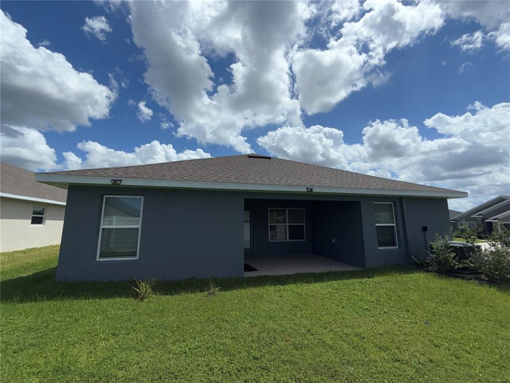 The exterior of a gray, single-story house features a covered patio and a grassy yard — 14921 TROPICAL VIOLET WAY, WIMAUMA, FL