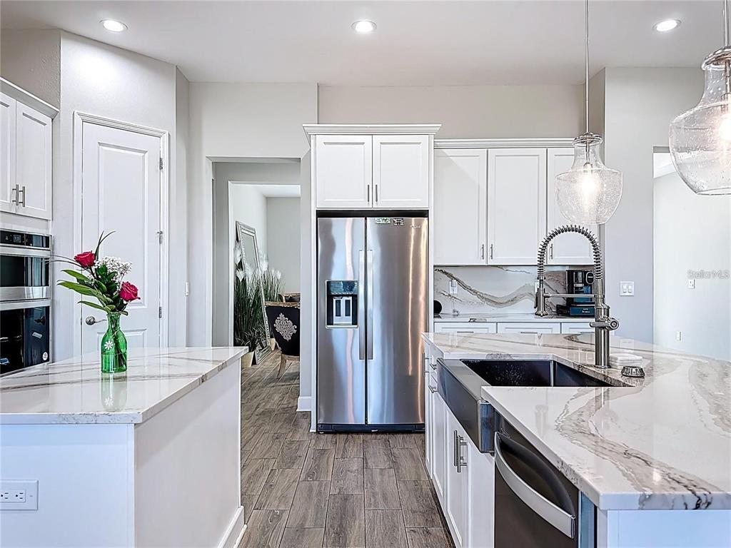 A modern kitchen features white cabinetry, stainless steel appliances, and a marble-topped island — 5216 LAKE VENICE DRIVE, WIMAUMA, FL