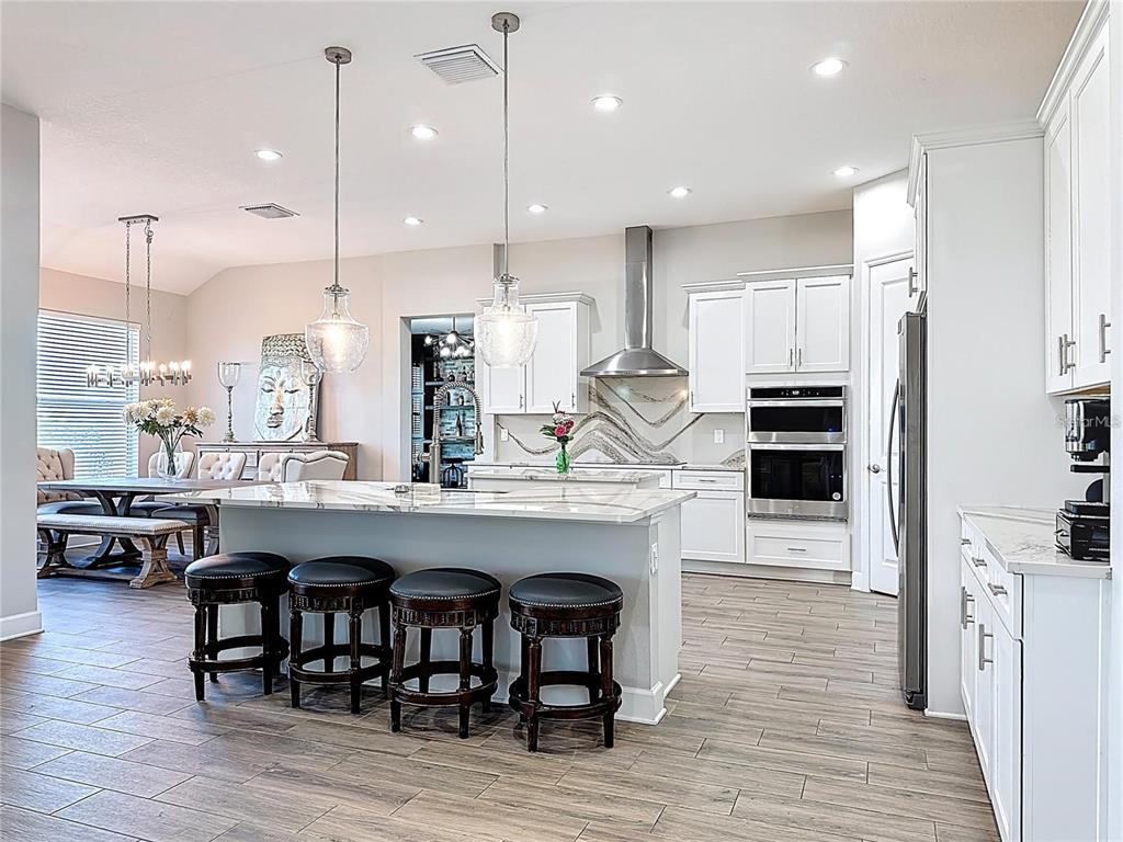 A modern kitchen features white cabinetry, a marble-topped island with four stools, and stainless appliances — 5216 LAKE VENICE DRIVE, WIMAUMA, FL