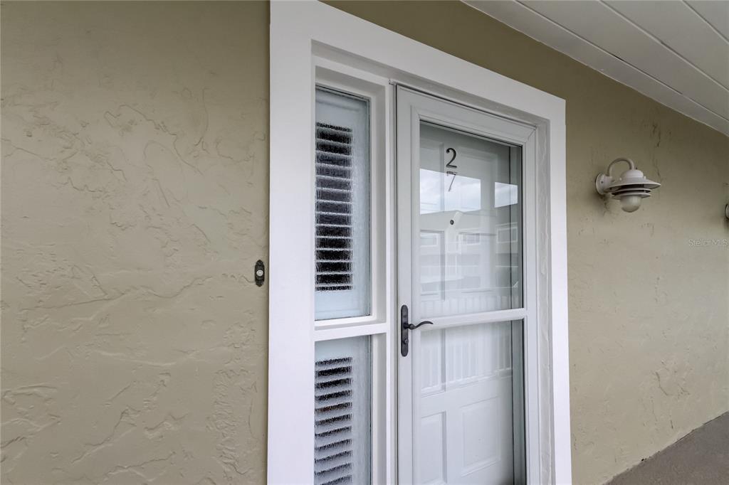 A white storm door with the number 27 on the glass is set in a wall — 433 PAULA DRIVE S UNIT 27, DUNEDIN, FL