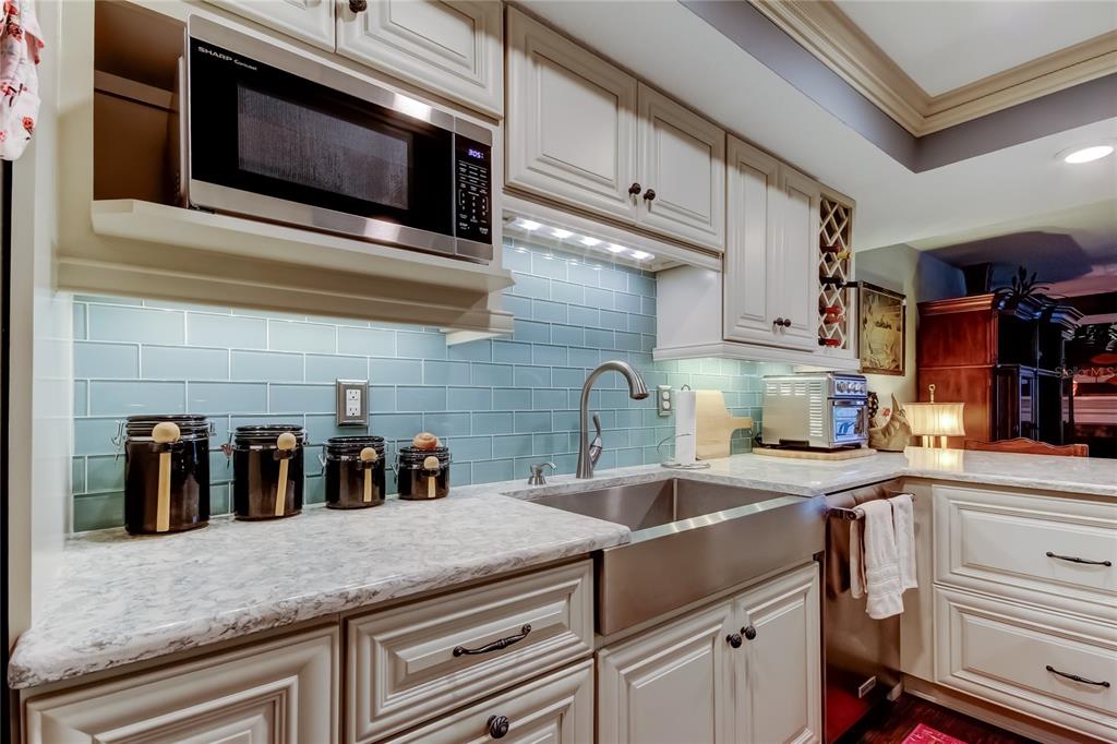 A kitchen features light-colored cabinets, a stainless steel farmhouse sink, and a blue subway tile backsplash — 433 PAULA DRIVE S UNIT 27, DUNEDIN, FL