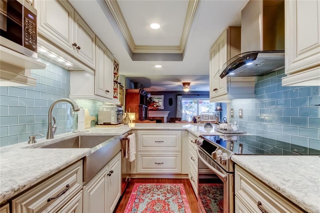 A galley kitchen features white cabinets, light countertops, a farmhouse sink, and blue subway tile — 433 PAULA DRIVE S UNIT 27, DUNEDIN, FL