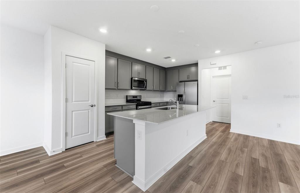 An open-concept living room and kitchen featuring a gray sectional, round coffee table, and patio — 9885 TRELLIS VINE WAY, PARRISH, FL