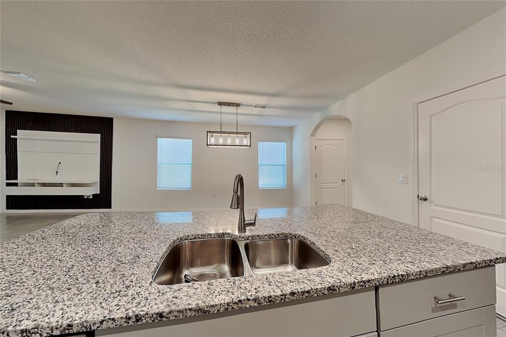 A kitchen island with a granite countertop and double sink overlooks a living area — 230 MEGHAN CIRCLE, DELAND, FL