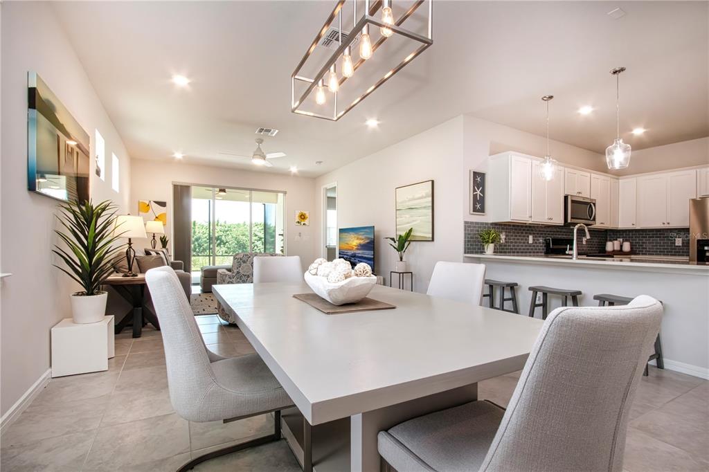 A dining room with a rectangular table and pendant lighting opens into a modern kitchen — 8427 OCEAN TIDES COVE, PARRISH, FL