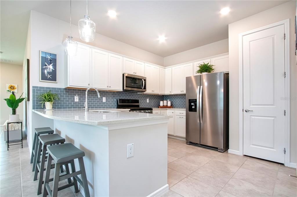 A kitchen features white cabinets, stainless steel appliances, a gray tile backsplash, and a breakfast bar — 8427 OCEAN TIDES COVE, PARRISH, FL