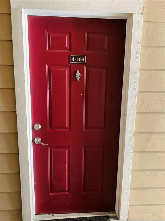 A red front door with a silver knocker and the number 4-104 is set in beige siding — 2025 ERVING CIRCLE UNIT 104, OCOEE, FL