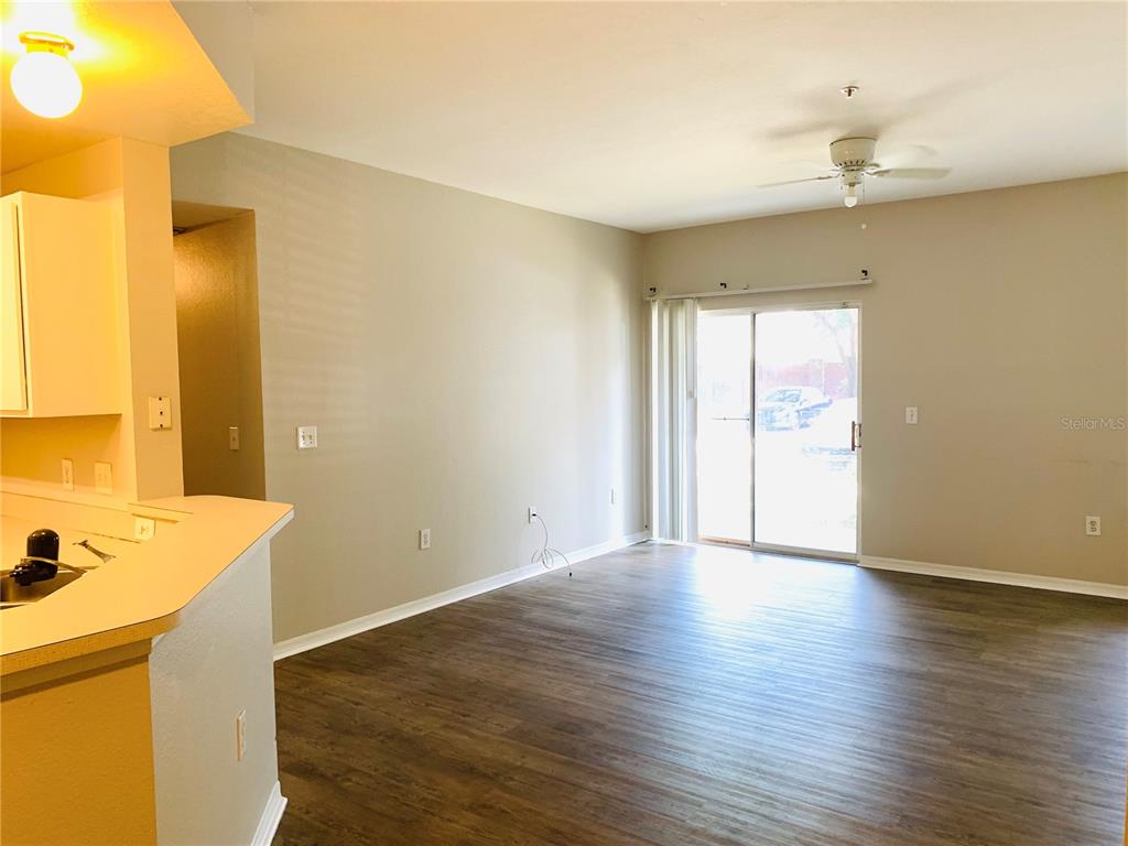 An empty living room features wood-look flooring, a ceiling fan, and a sliding glass door — 2025 ERVING CIRCLE UNIT 104, OCOEE, FL