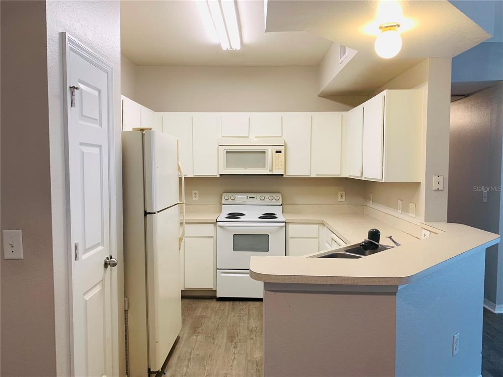 A kitchen with white cabinets, white appliances, and a peninsula counter with a sink — 2025 ERVING CIRCLE UNIT 104, OCOEE, FL