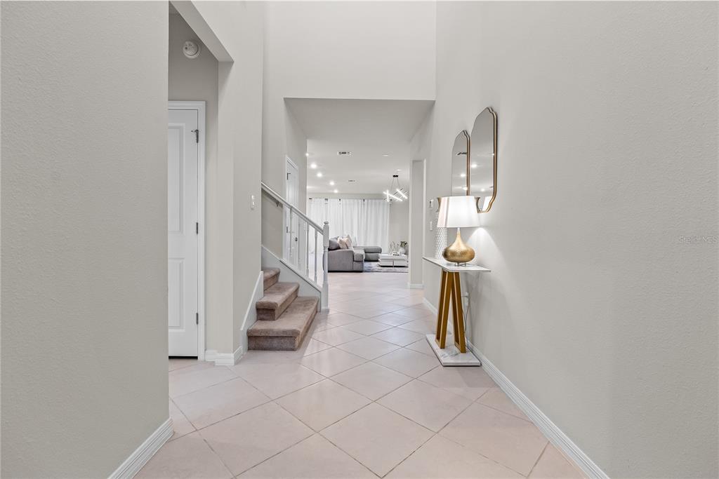 A bright entryway features tile flooring, a staircase with carpeted steps, and a console table — 16208 SAINT MARTIN STREET, CLERMONT, FL