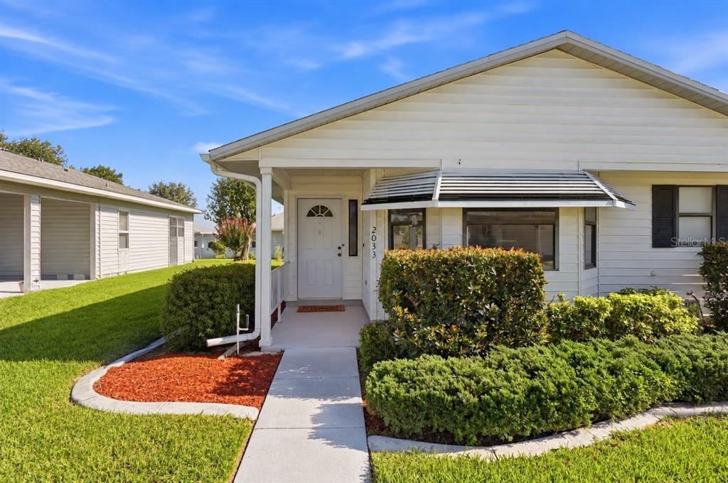 A white single-story house with a large tree in the front yard and landscaped bushes — 2033 LONG BOAT DRIVE, LAKELAND, FL