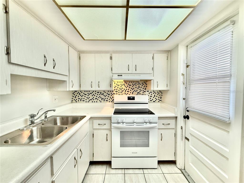 A kitchen with white cabinets, white appliances, a tiled backsplash, and a drop ceiling light — 6105 CORAL WAY, BRADENTON, FL