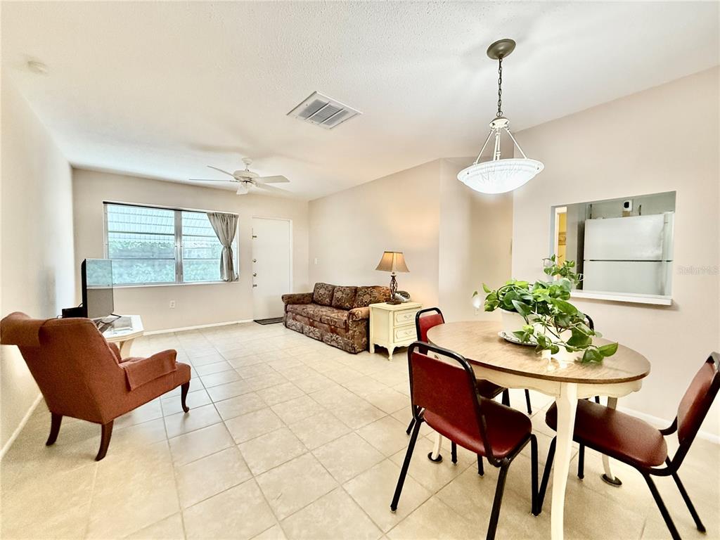 A living and dining area features tile flooring, a ceiling fan, and a pass-through kitchen window — 6105 CORAL WAY, BRADENTON, FL