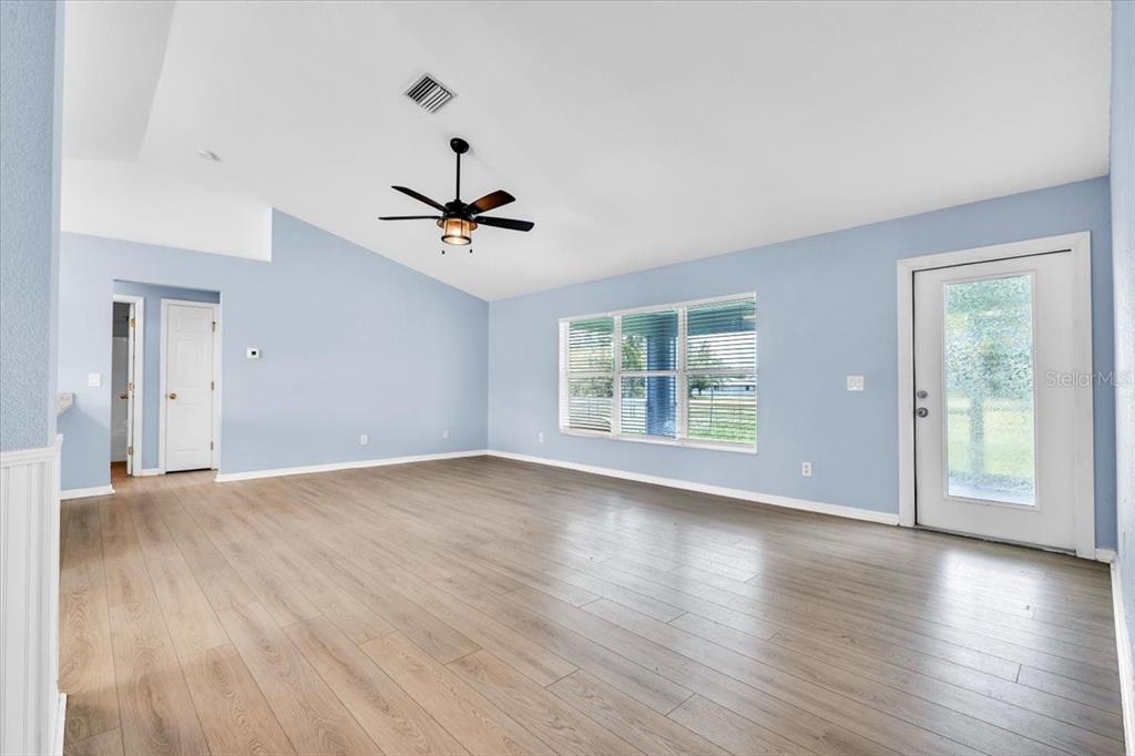 An empty living room features light blue walls, wood-look flooring, a ceiling fan, and windows — 1708 BLUE LAKE CIRCLE, PUNTA GORDA, FL