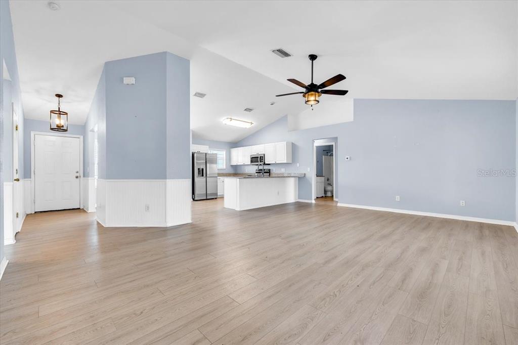 An open-concept living area features light blue walls, wood-look flooring, and a kitchen with white cabinets — 1708 BLUE LAKE CIRCLE, PUNTA GORDA, FL