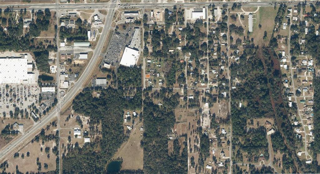 This aerial view shows a residential area with scattered houses, wooded lots, and nearby commercial buildings — 310 FLORIDA DRIVE, PALATKA, FL